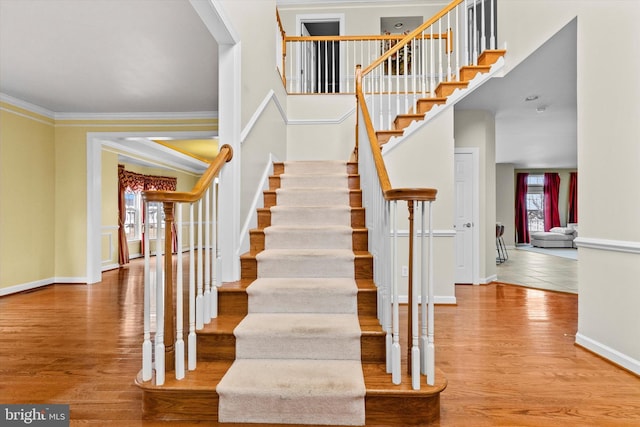 stairs featuring baseboards, a high ceiling, wood finished floors, and crown molding