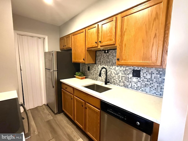 kitchen with a sink, light wood-style floors, light countertops, appliances with stainless steel finishes, and tasteful backsplash