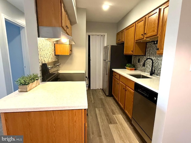 kitchen with under cabinet range hood, wood finished floors, a sink, appliances with stainless steel finishes, and brown cabinets