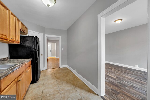 kitchen with freestanding refrigerator, light tile patterned flooring, a sink, dark stone counters, and baseboards