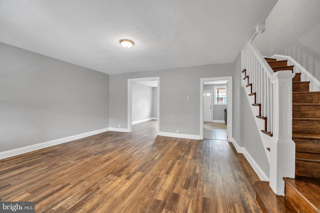 unfurnished room featuring dark wood finished floors, baseboards, and stairs