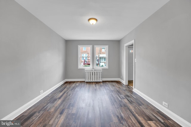 spare room featuring baseboards, dark wood-style flooring, and radiator