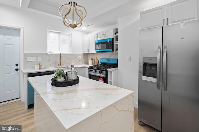 kitchen with a tray ceiling, light wood-style flooring, tasteful backsplash, and appliances with stainless steel finishes