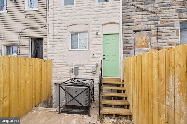property entrance with stone siding, cooling unit, and fence