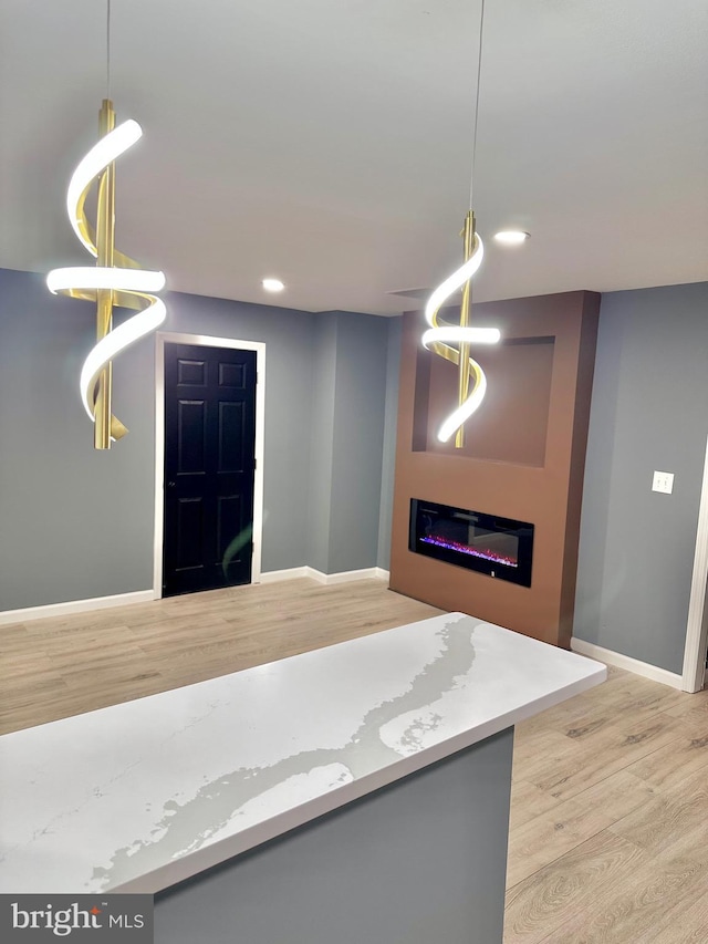 kitchen with wood finished floors, a glass covered fireplace, decorative light fixtures, and baseboards