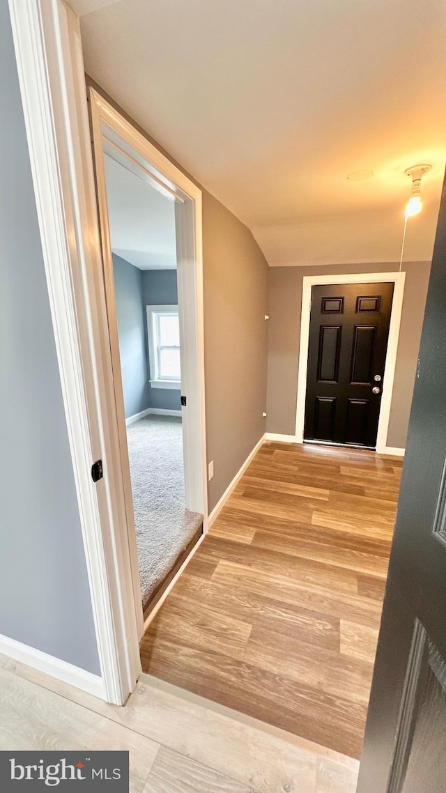 hallway with lofted ceiling, light wood-style floors, and baseboards