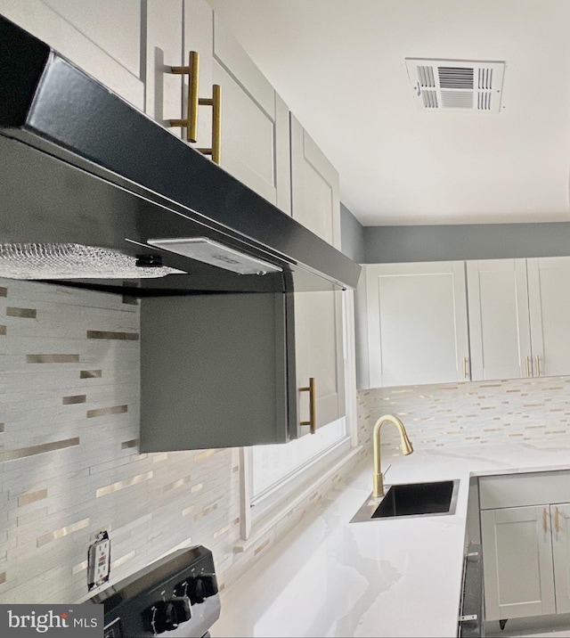 kitchen with tasteful backsplash, visible vents, light countertops, under cabinet range hood, and a sink