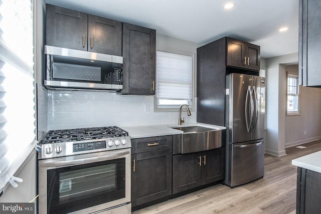 kitchen featuring stainless steel appliances, a sink, baseboards, light wood-type flooring, and tasteful backsplash