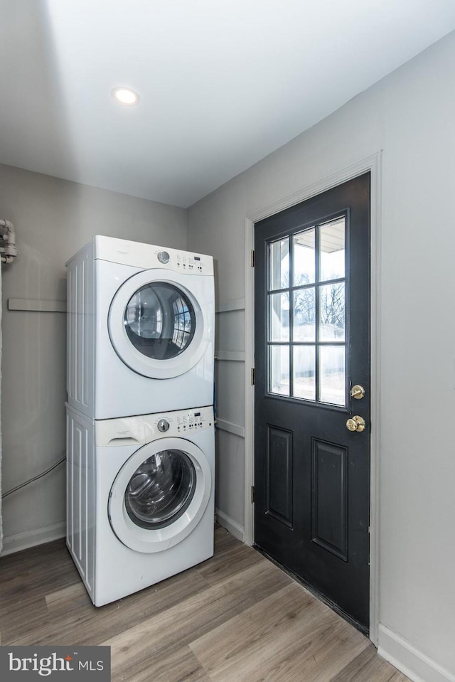 laundry area featuring wood finished floors, stacked washer and clothes dryer, baseboards, and laundry area