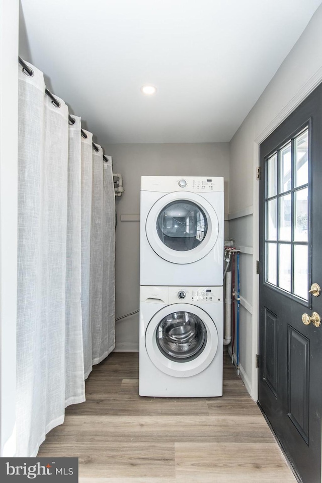 clothes washing area featuring stacked washer / drying machine, laundry area, and wood finished floors