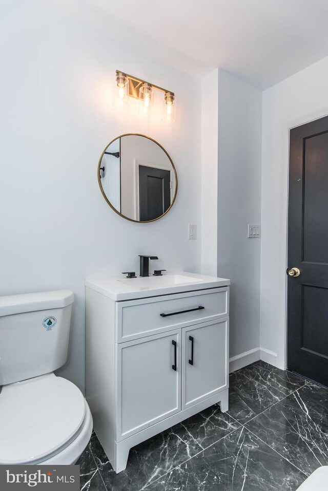 half bath with toilet, marble finish floor, baseboards, and vanity