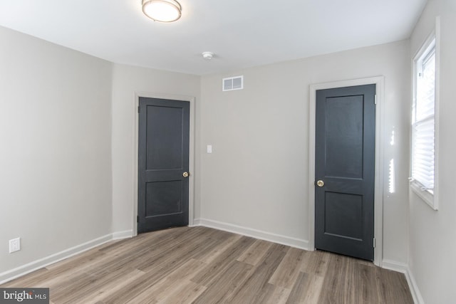 unfurnished room with light wood-type flooring, visible vents, and baseboards