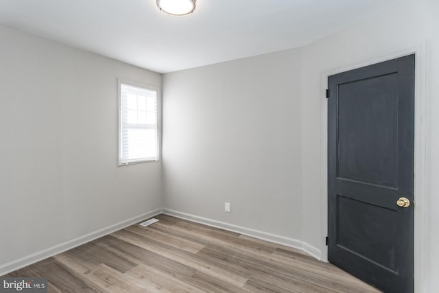 empty room with wood finished floors, visible vents, and baseboards