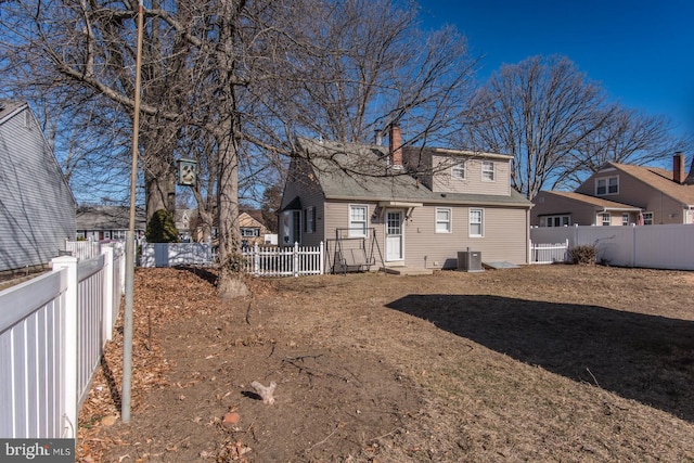 rear view of property featuring central air condition unit, a fenced backyard, and a chimney