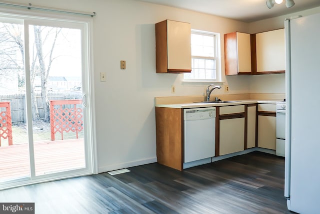 kitchen featuring white appliances, a sink, baseboards, light countertops, and dark wood finished floors