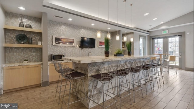 kitchen with visible vents, lofted ceiling, stainless steel microwave, light wood-style floors, and light brown cabinets