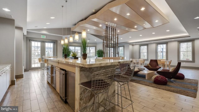 kitchen featuring light stone counters, a kitchen breakfast bar, a large island, wood tiled floor, and pendant lighting