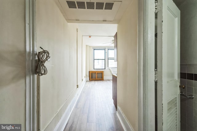 hall with radiator heating unit, wood finished floors, and visible vents