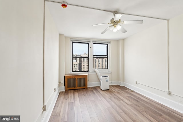 empty room featuring ceiling fan, radiator heating unit, wood finished floors, and baseboards