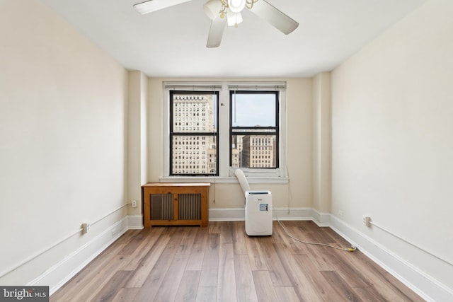 empty room featuring radiator, ceiling fan, baseboards, and wood finished floors