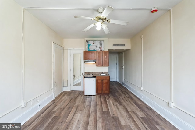 kitchen featuring under cabinet range hood, dark wood-style flooring, visible vents, brown cabinets, and dishwasher