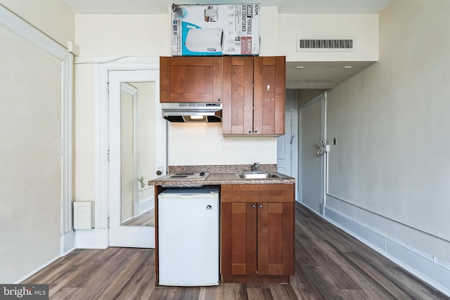 kitchen with dark wood-style flooring, a sink, visible vents, and under cabinet range hood