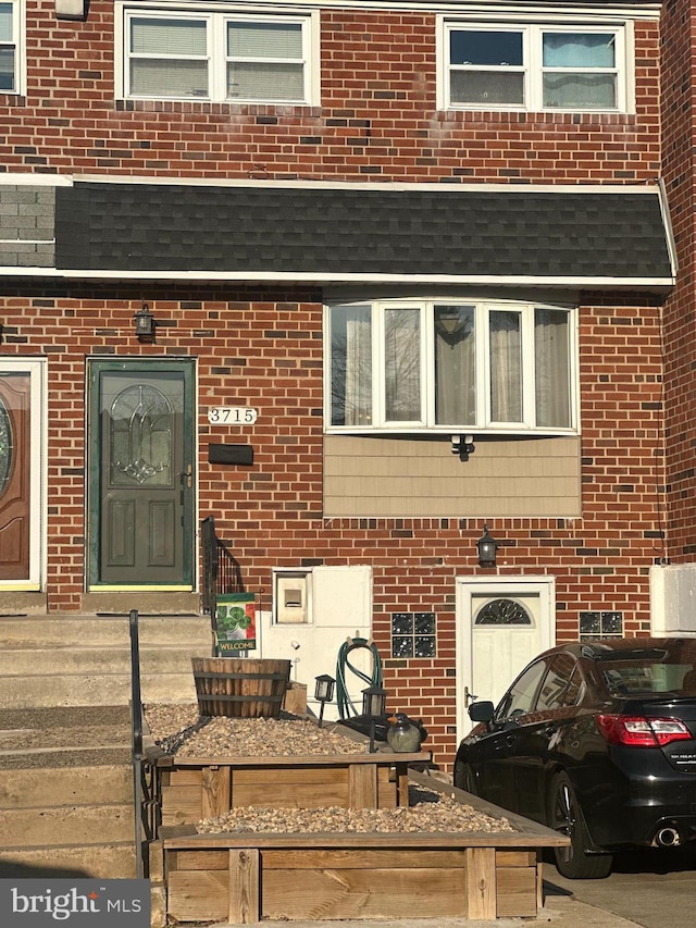 view of exterior entry with a shingled roof and brick siding