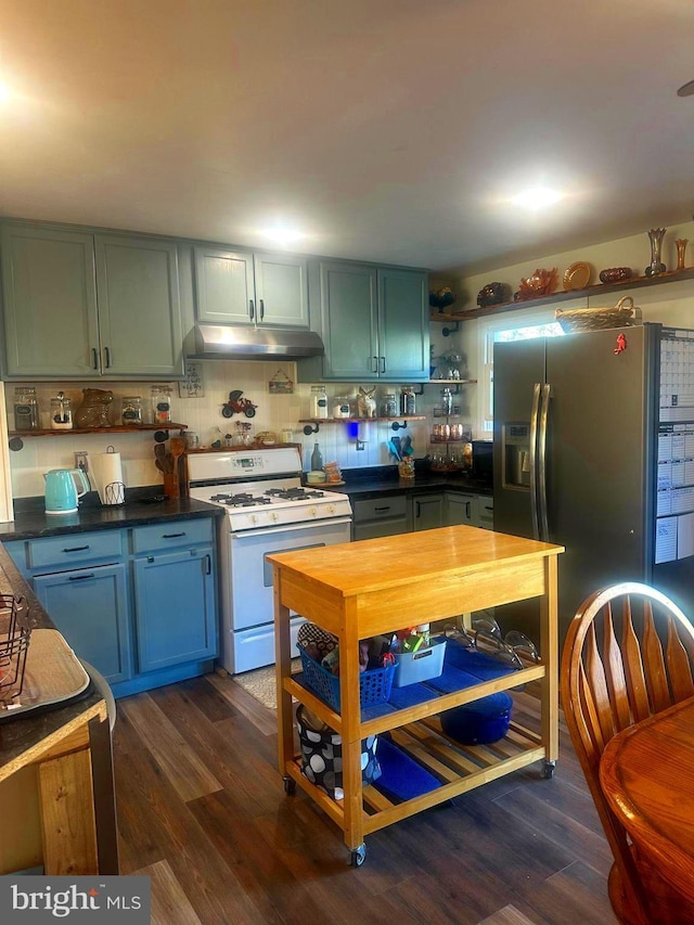 kitchen with white gas stove, under cabinet range hood, dark wood-style flooring, open shelves, and dark countertops