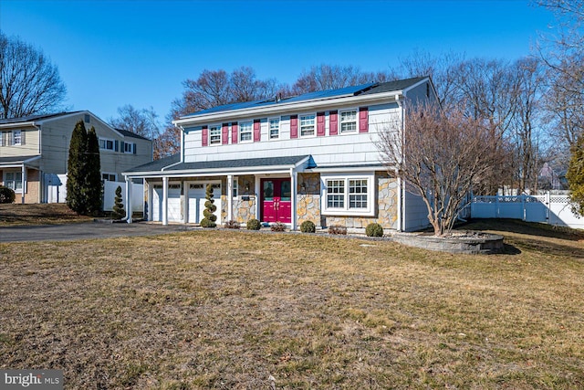 view of front of property with aphalt driveway, covered porch, a front yard, roof mounted solar panels, and fence