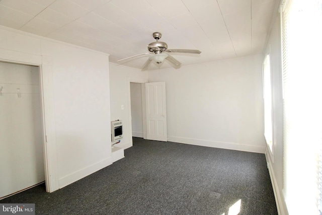 unfurnished bedroom with heating unit, a ceiling fan, baseboards, and dark colored carpet