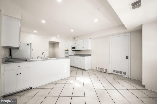 kitchen with a peninsula, white appliances, a sink, and visible vents