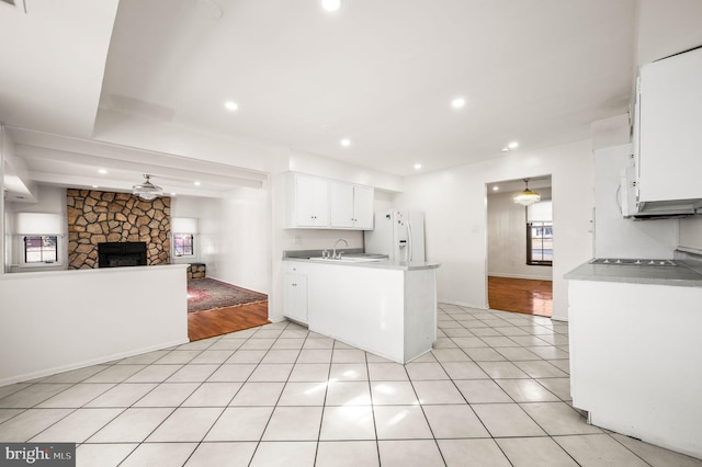 kitchen with light tile patterned floors, white cabinets, open floor plan, a peninsula, and white fridge with ice dispenser