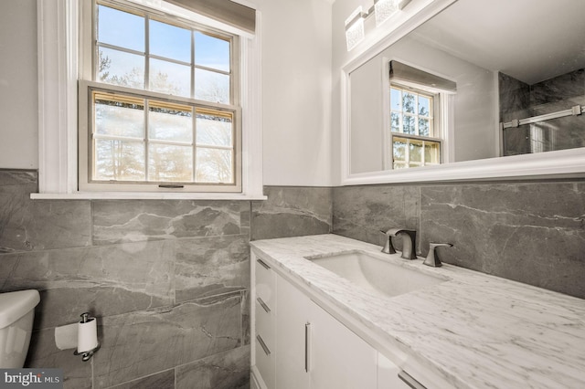 bathroom with toilet, vanity, and tile walls