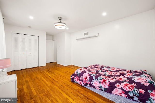 bedroom with a closet, wood finished floors, visible vents, and recessed lighting