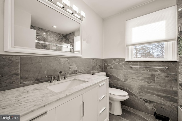 bathroom featuring wainscoting, toilet, walk in shower, vanity, and tile walls