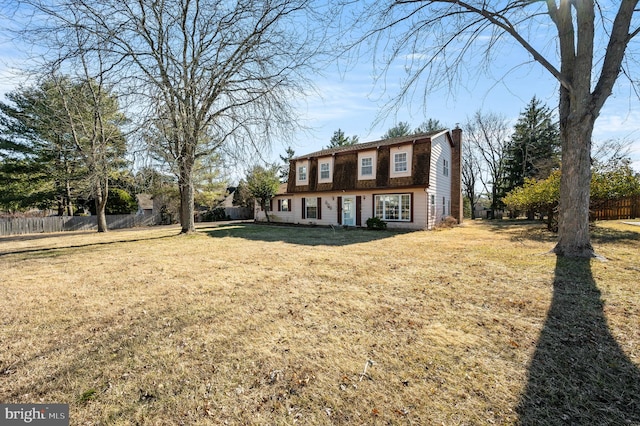 dutch colonial featuring a shingled roof, a gambrel roof, a chimney, fence, and a front yard