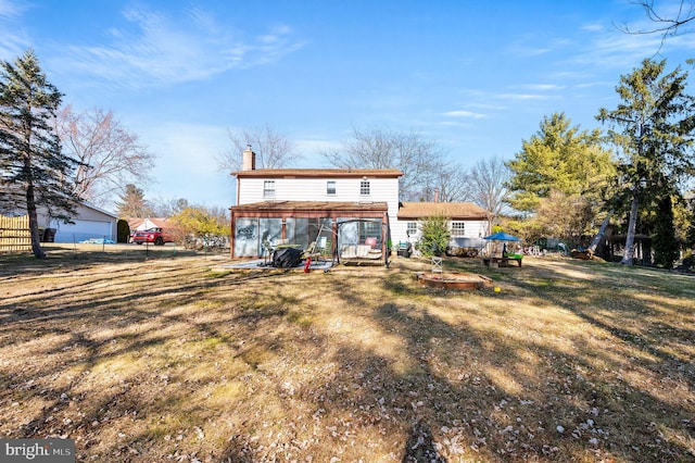 back of property with a chimney, a lawn, a fire pit, and fence