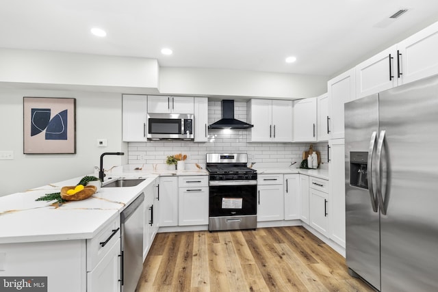 kitchen with a peninsula, a sink, appliances with stainless steel finishes, wall chimney range hood, and decorative backsplash