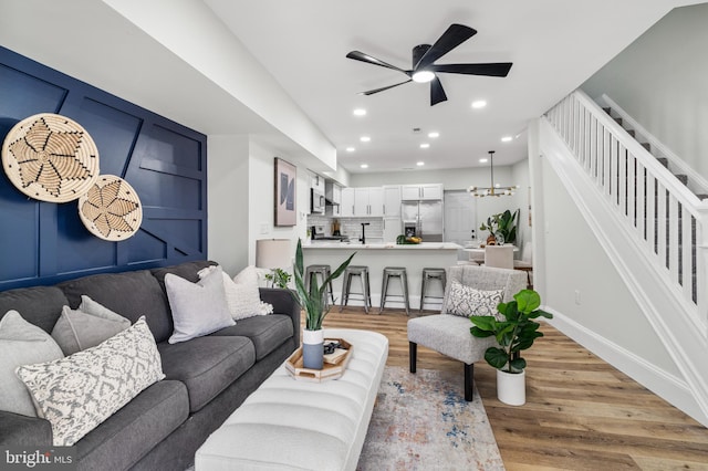 living room with baseboards, light wood-style flooring, ceiling fan, stairway, and recessed lighting