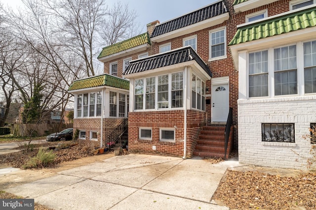 exterior space with a sunroom, mansard roof, and brick siding