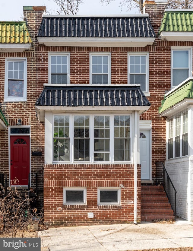 view of property featuring entry steps, brick siding, and mansard roof