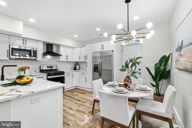 kitchen featuring backsplash, stainless steel appliances, light wood-type flooring, wall chimney range hood, and a sink