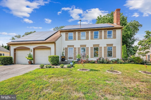 colonial home featuring solar panels, a chimney, aphalt driveway, an attached garage, and a front lawn