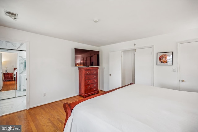 bedroom featuring ensuite bathroom, wood finished floors, visible vents, and baseboards