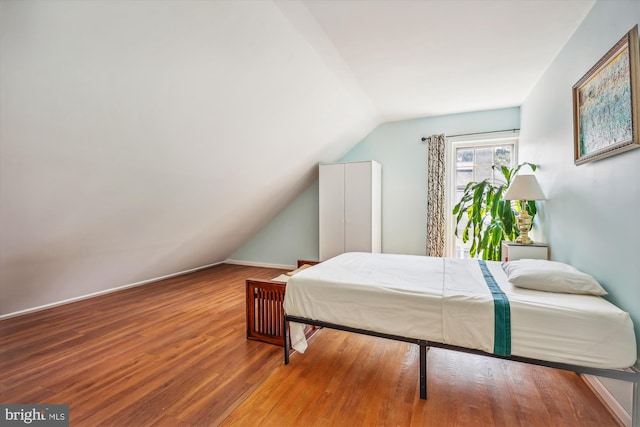 bedroom with vaulted ceiling, baseboards, and wood finished floors