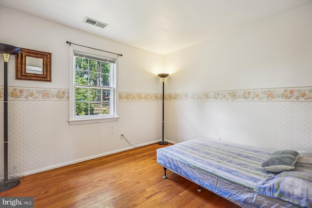 bedroom with wallpapered walls, baseboards, visible vents, wainscoting, and wood finished floors