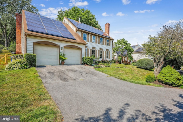 colonial home with a garage, a front lawn, a chimney, and aphalt driveway