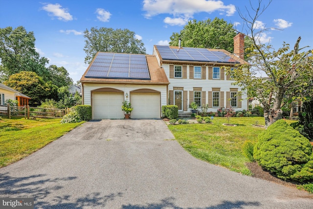 colonial house with an attached garage, solar panels, fence, driveway, and a front yard