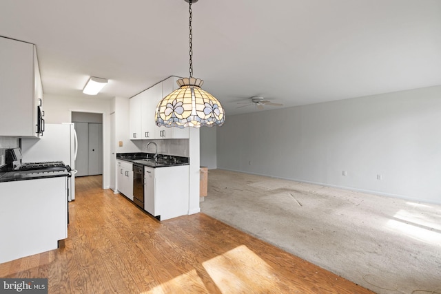 kitchen with a sink, white cabinetry, open floor plan, light wood finished floors, and dark countertops