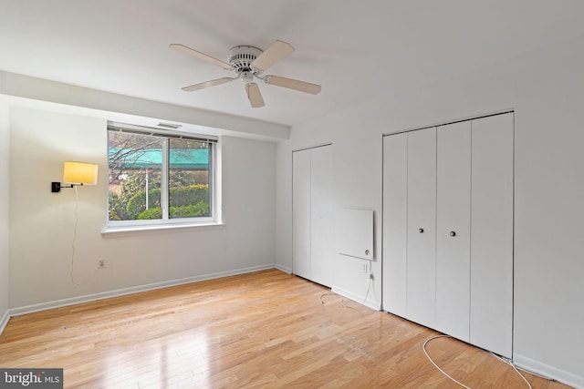 unfurnished bedroom featuring wood finished floors, two closets, a ceiling fan, and baseboards